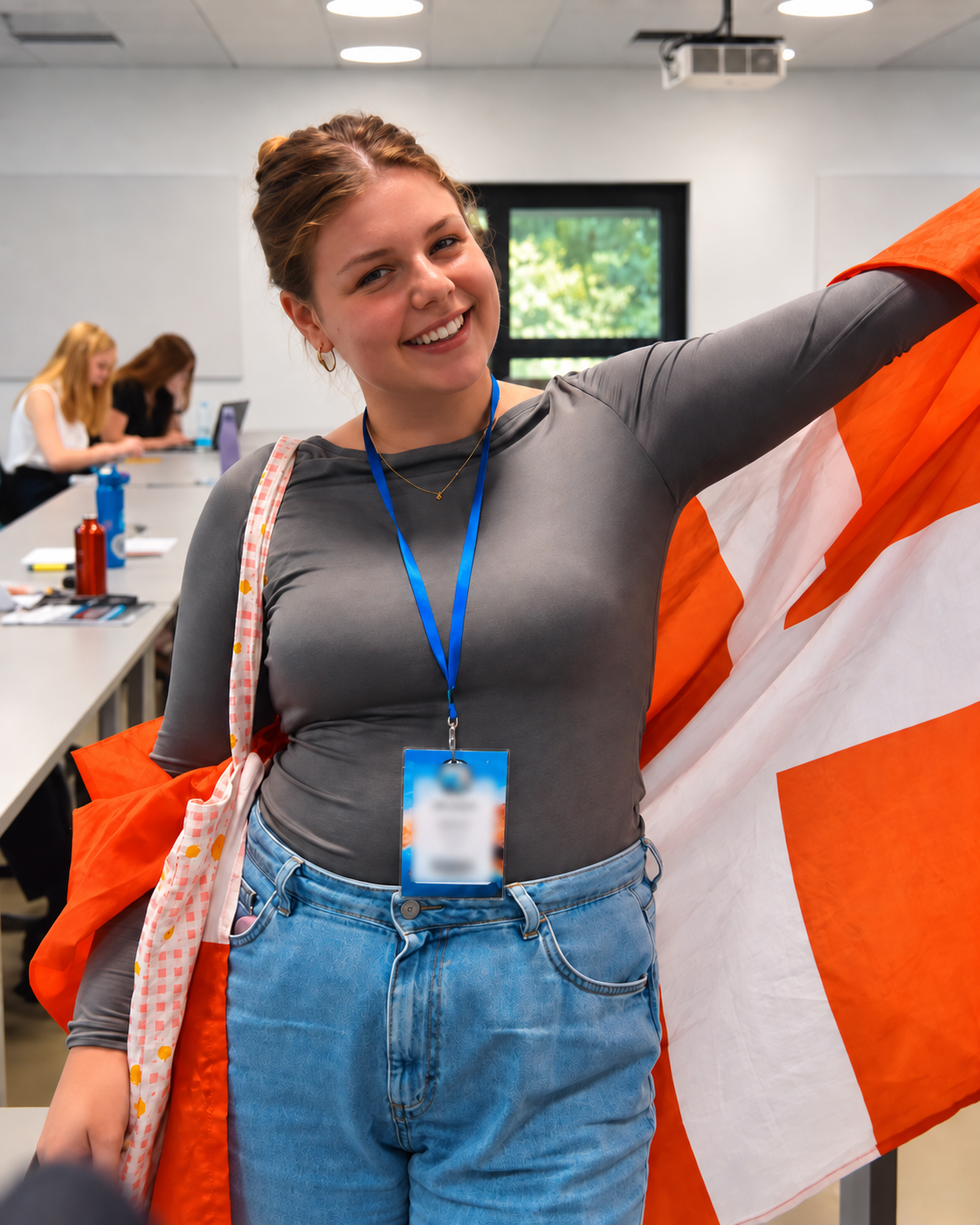 A smiling student in a classroom holding a Danish flag