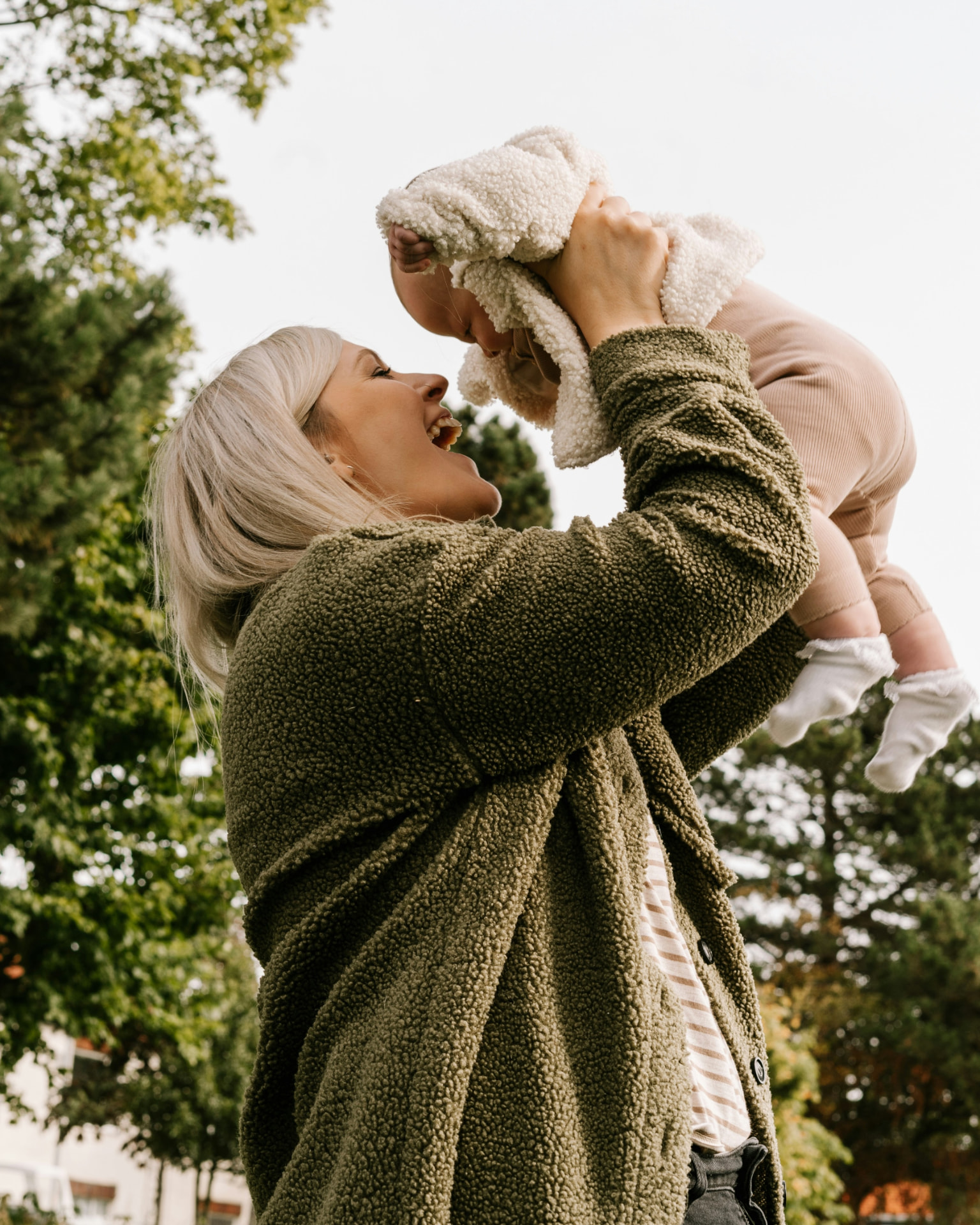 A mother smiling as she lifts her baby into the air outside