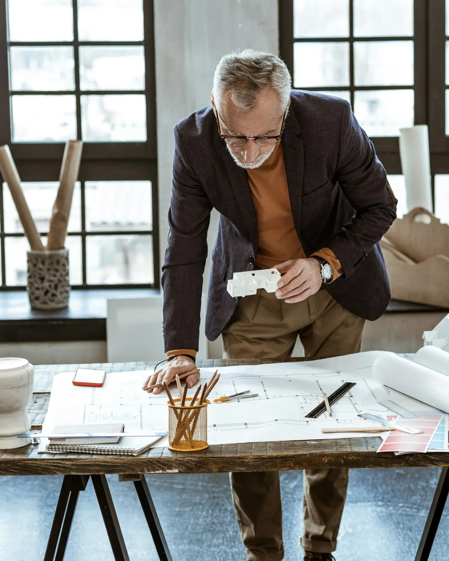 A man holding a small architectural model over blueprints on a desk